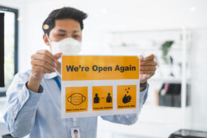 Man holding sign in business that says: we're opening again